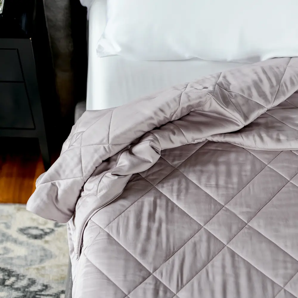 The corner of a made bed with the quilted Lightweight Blanket folded back over white sheets