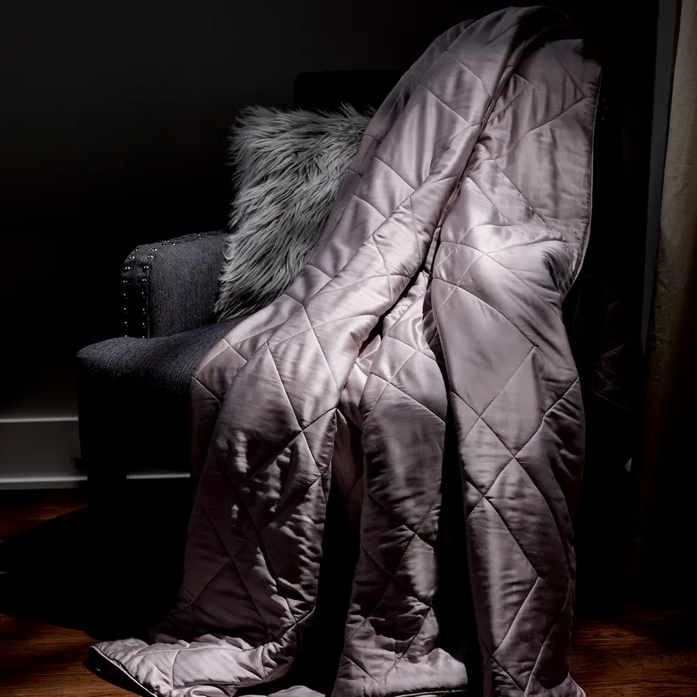 The quilted Luxome Lightweight Blanket draped over an armchair in a dark room, hanging flat
