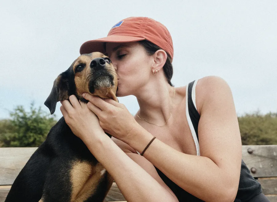A dog owner holding and kissing her dog outdoors