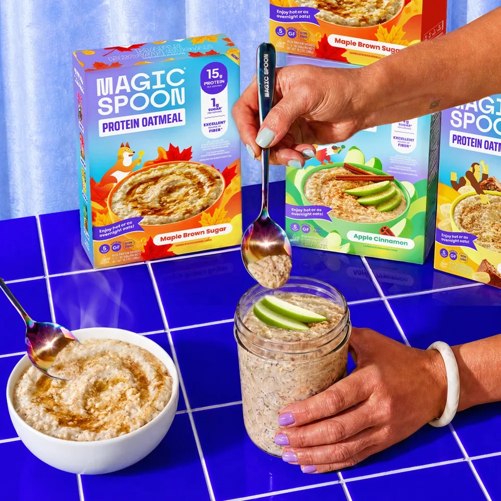 A bowl of hot Magic Spoon oatmeal steaming next to a glass jar of overnight oats, with boxes of the three flavors behind