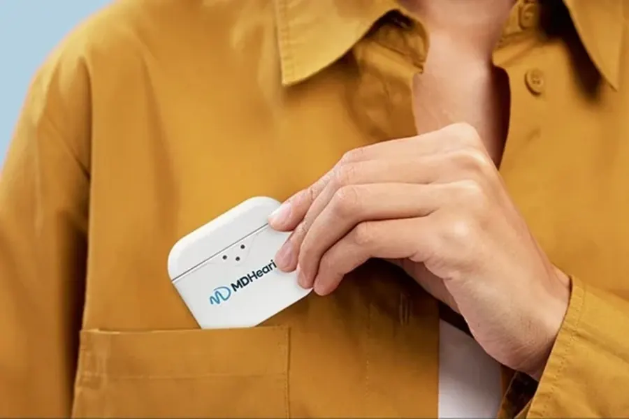 A hand holding the small round MDHearing charging case