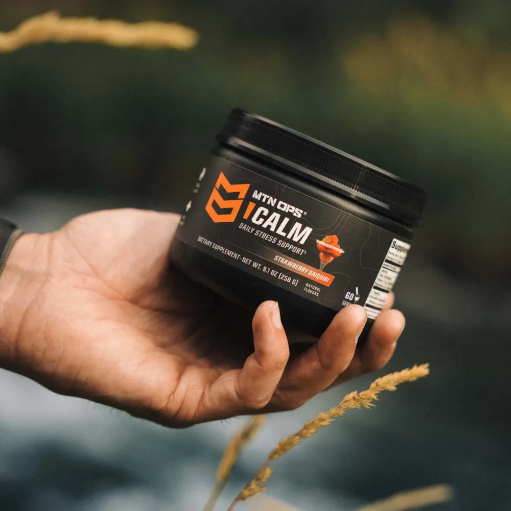 A hand holding a tub of MTN OPS CALM in a field
