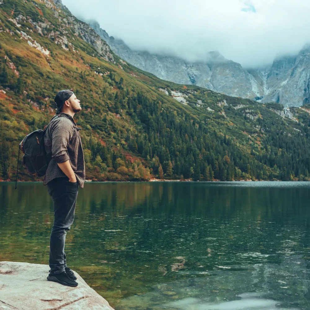 A man standing at the edge of a mountain lake