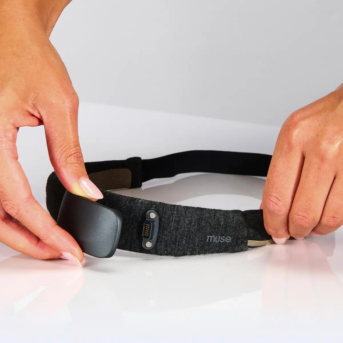 Two hands holding the Muse headband open, showing the flexible fabric strap and the sensor housing