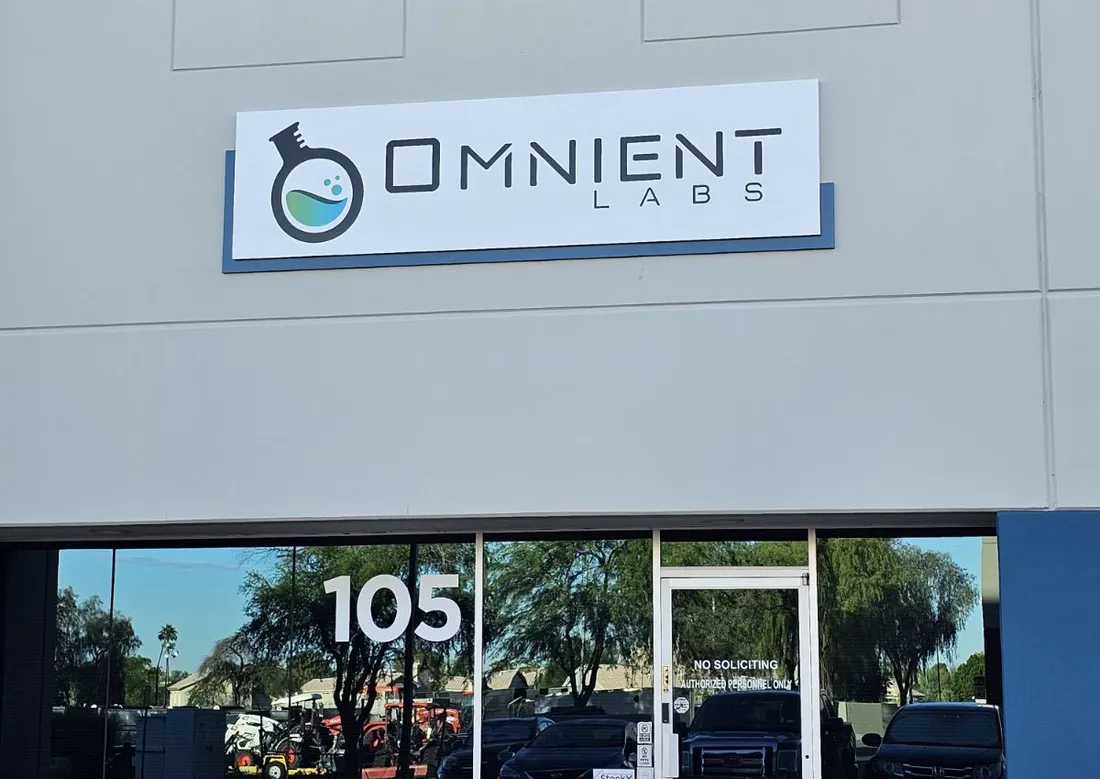 Exterior of a light industrial unit in Tempe, Arizona, with a wall-mounted sign reading Omnient Labs above a glass door marked with the suite number 105