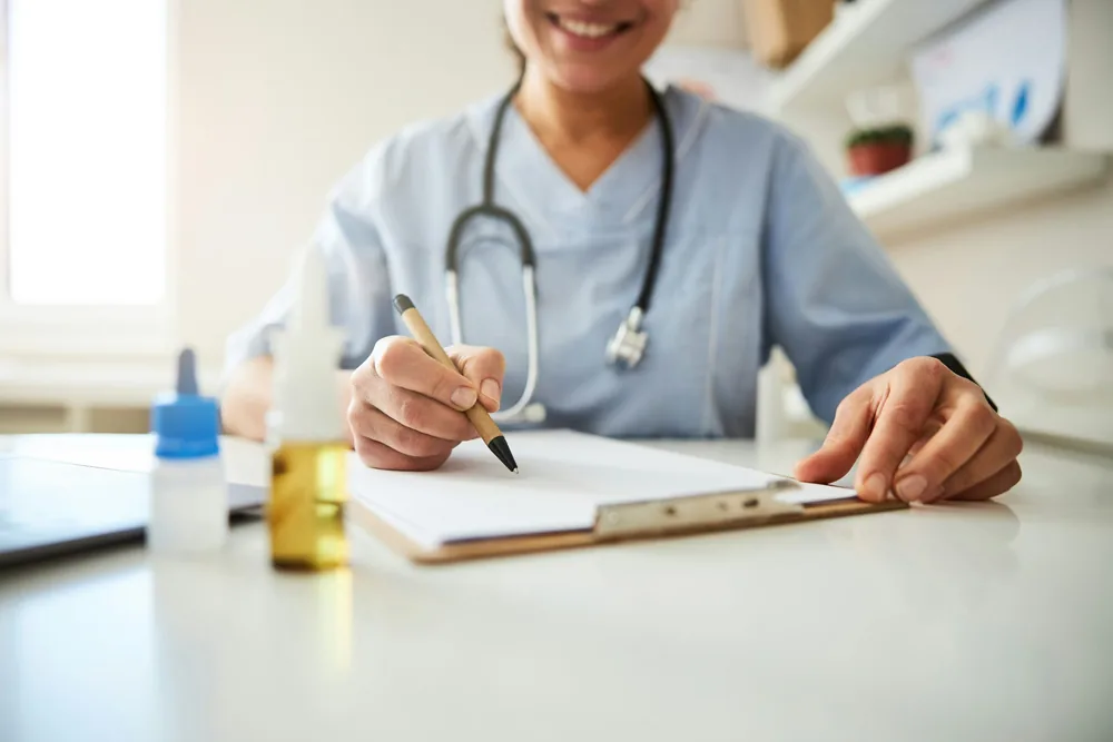 A clinician in scrubs writing notes at a desk