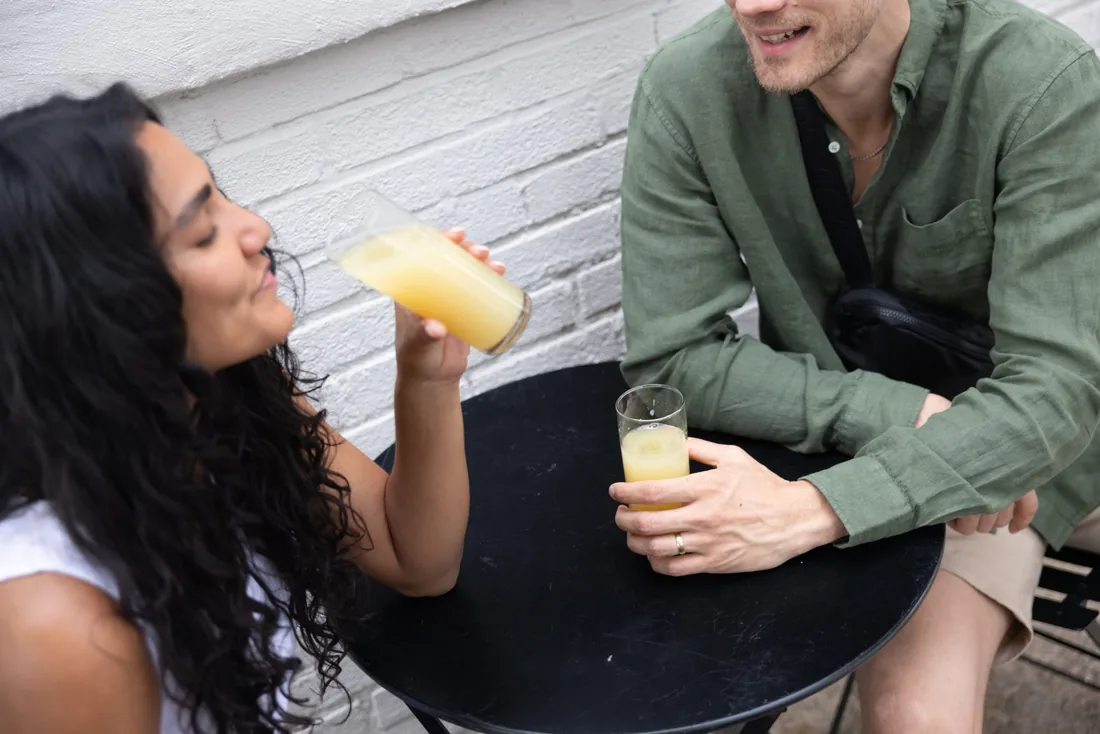Two people sitting at an outdoor table with glasses of a NOVOS drink