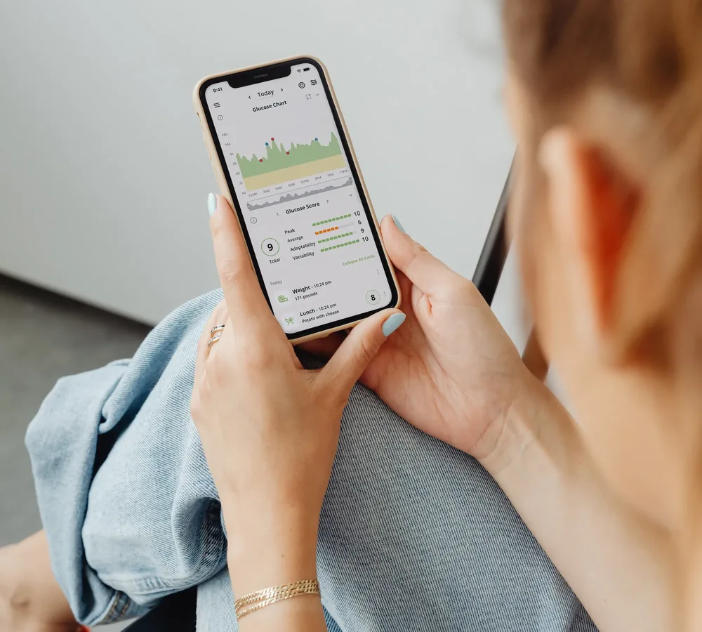 A person holding a phone showing the Nutrisense glucose chart and glucose score for the day.