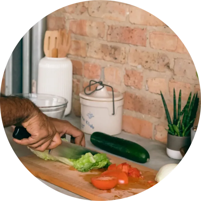 Hands chopping lettuce and tomatoes on a wooden board in a home kitchen.