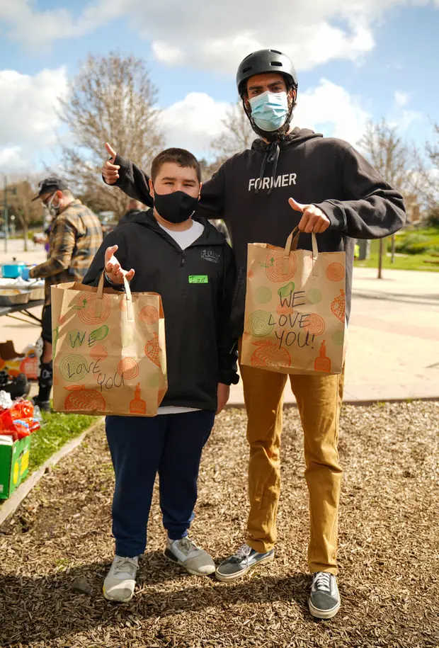 Two Meals on Onewheels volunteers holding paper bags of supplies.