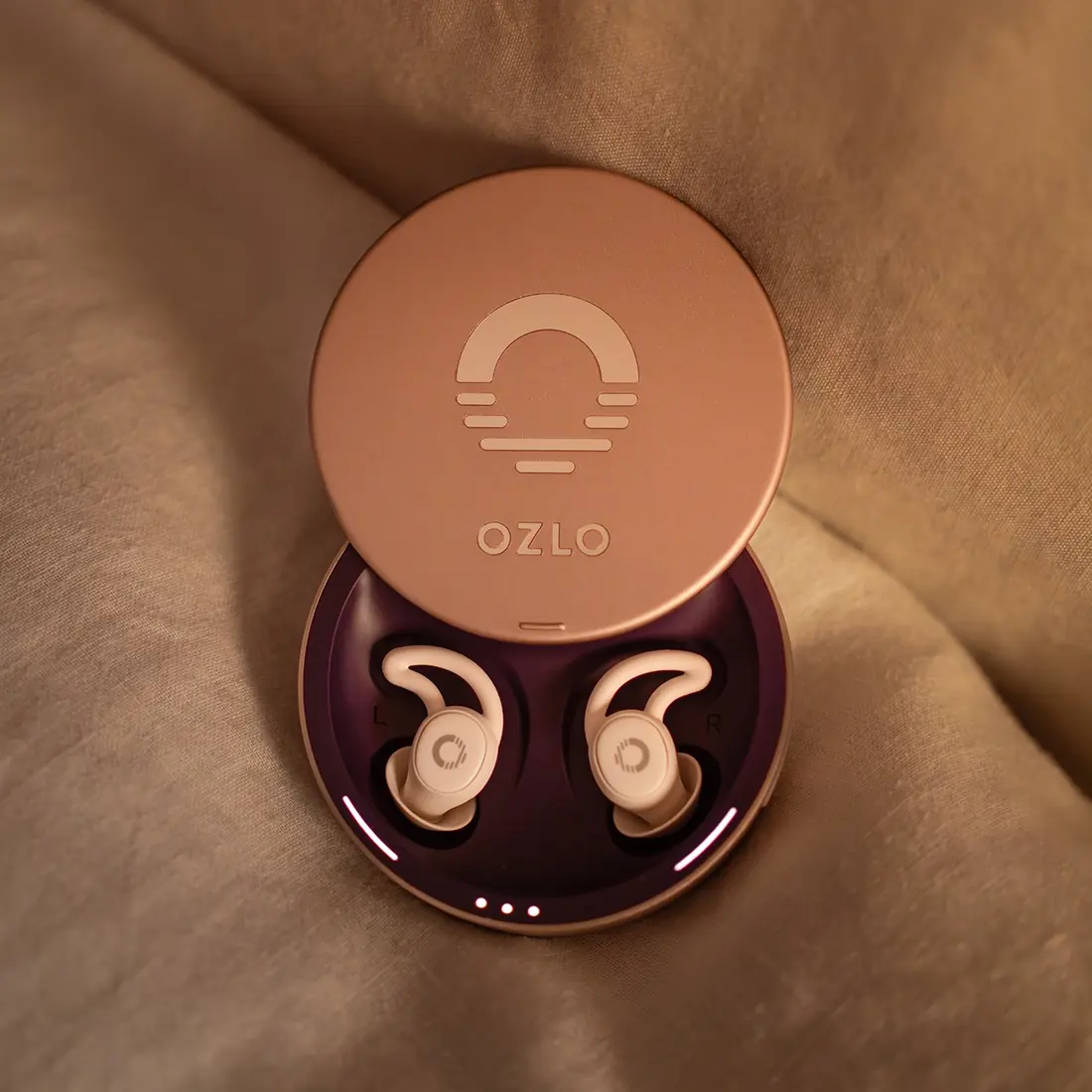 The Ozlo charging case open on bedding with the two sleep earbuds inside