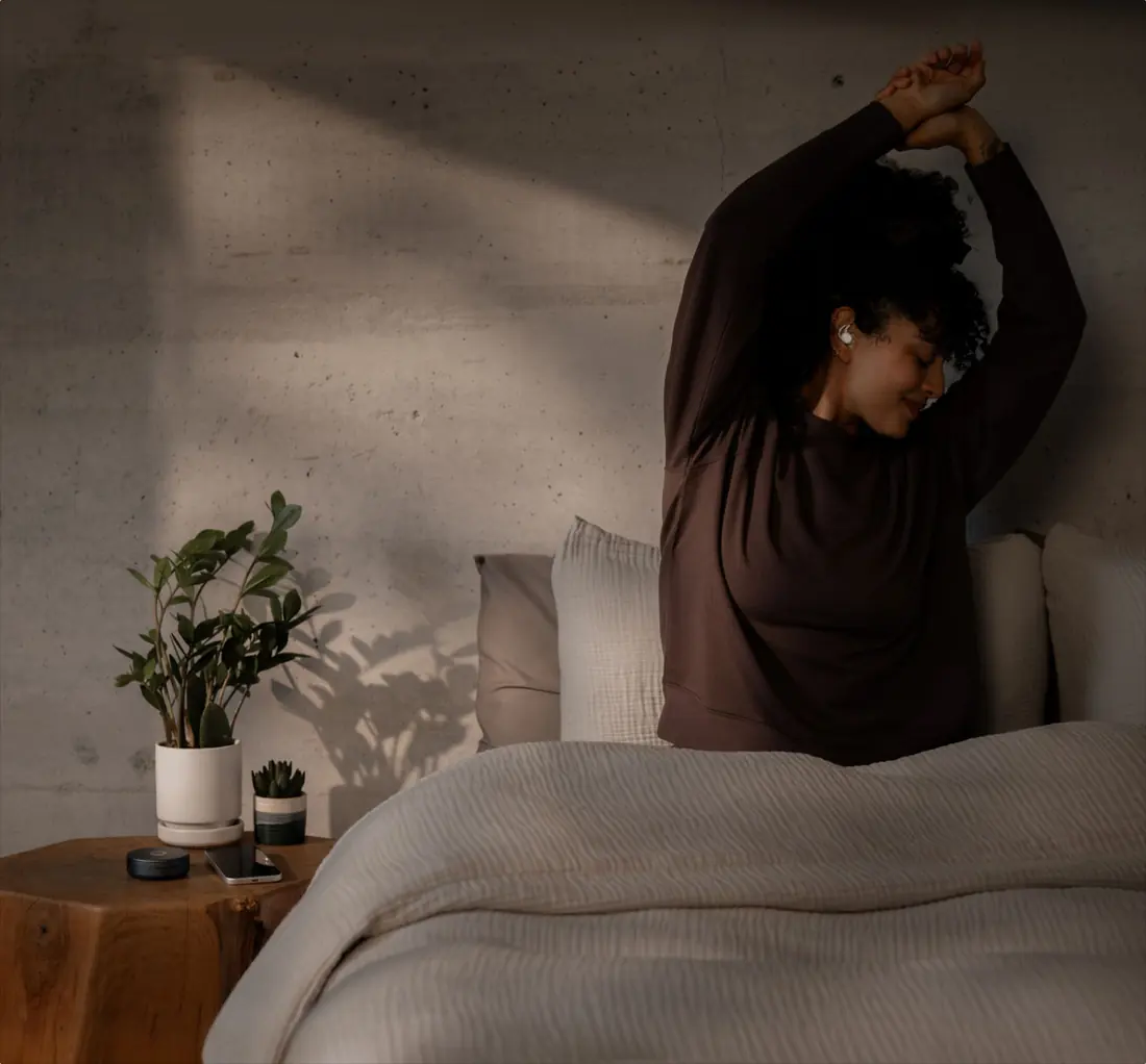 A woman waking up and stretching in bed in morning light