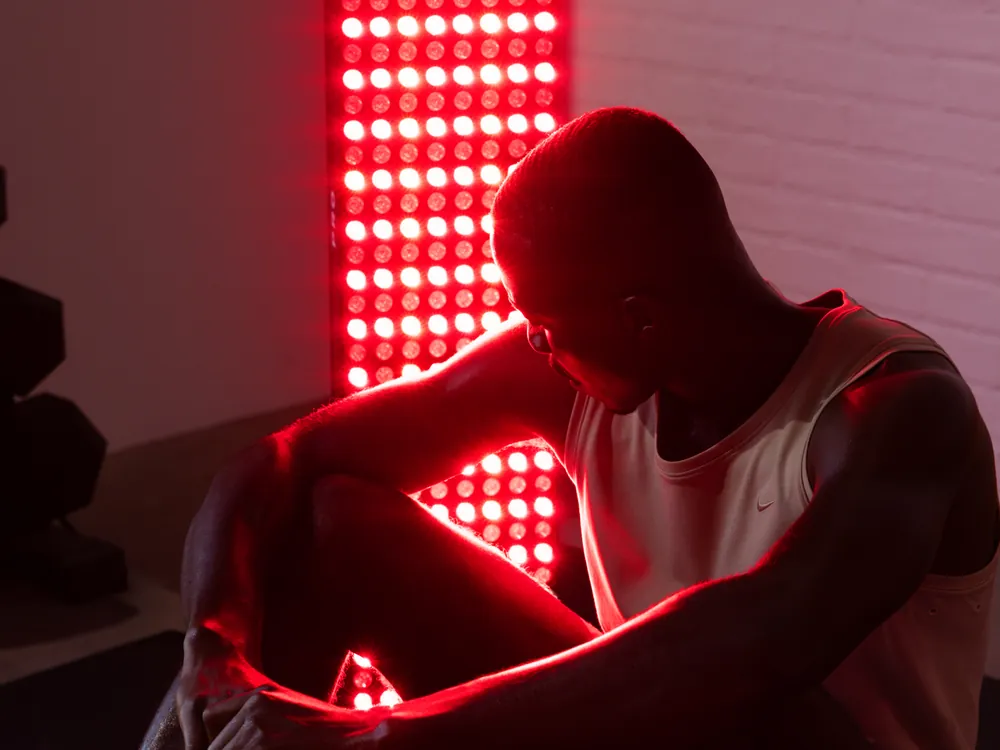 A man sitting on the floor beside a lit BIOMAX PRO panel, with the beam falling brightly on his near side and fading across his body