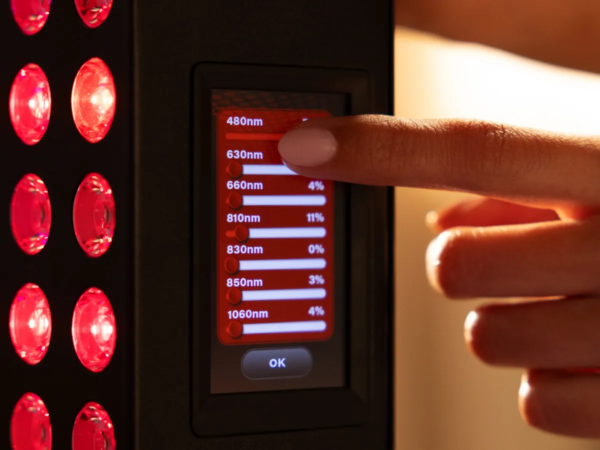 A finger on the BIOMAX PRO touchscreen, showing individual output percentages for 480, 630, 660, 810, 830, 850 and 1060 nanometer channels