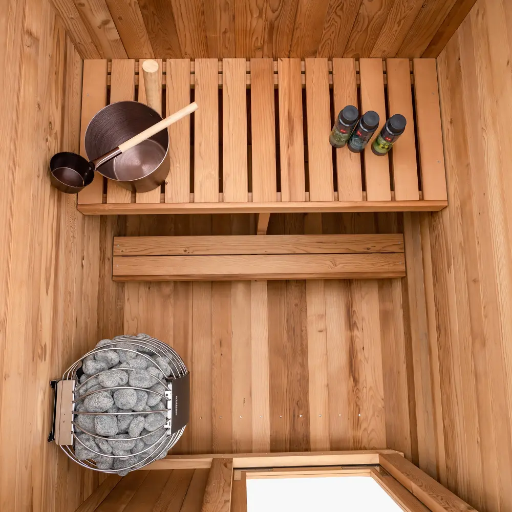 Overhead view inside a finished Duo sauna showing slatted benches, tongue and groove wall panels and the stone heater