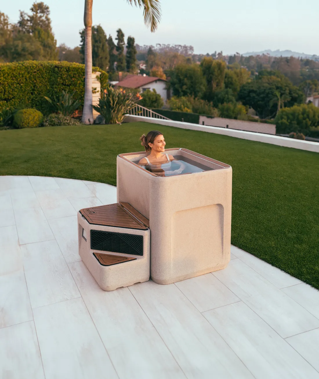 Woman in a Renu Therapy Vero cold plunge in Estonian Sandstone finish on a garden terrace
