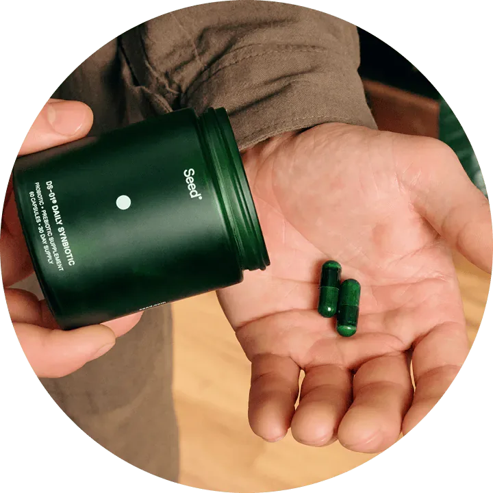 A hand tipping two green capsules out of the DS-01 jar into an open palm