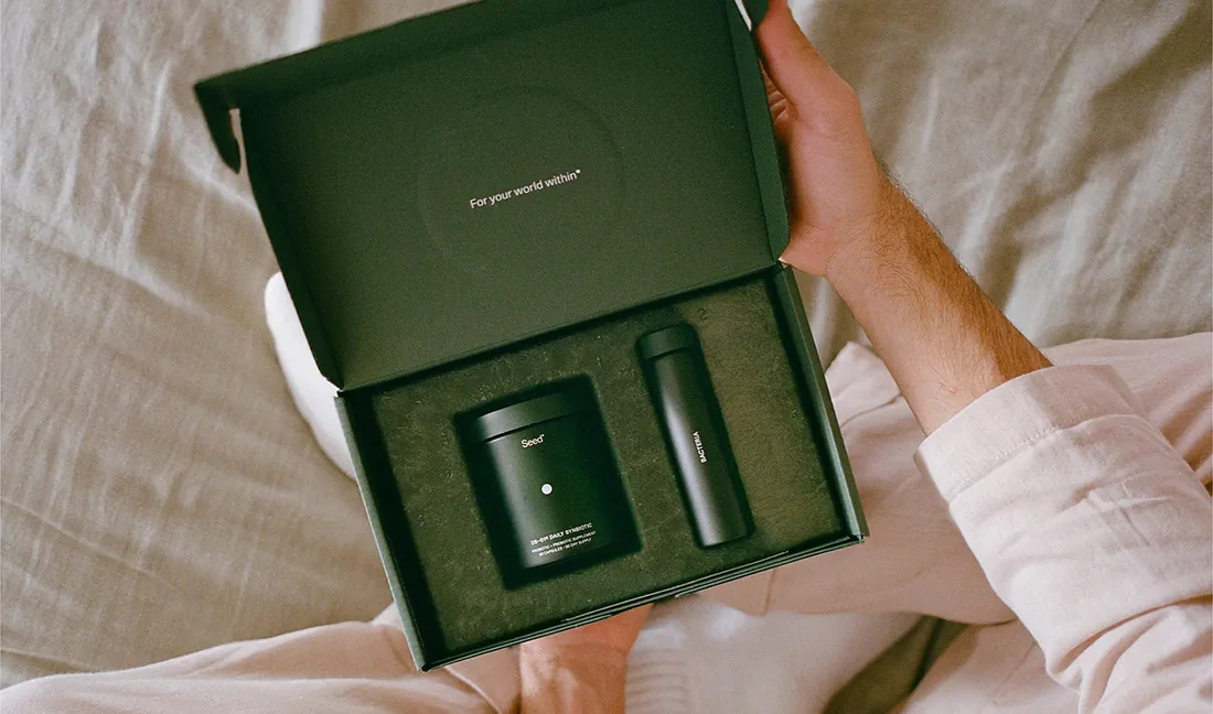 Two hands opening the DS-01 welcome kit box, holding a glass jar and a travel vial