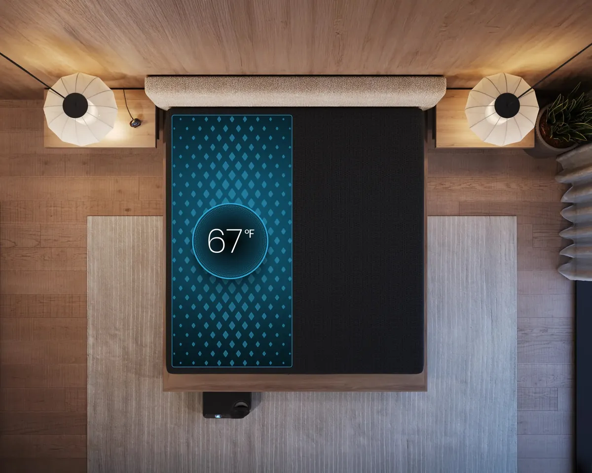A bed seen from above, one half of the mattress covered by a pad with a visible grid of water channels, and a temperature dial reading 67 degrees