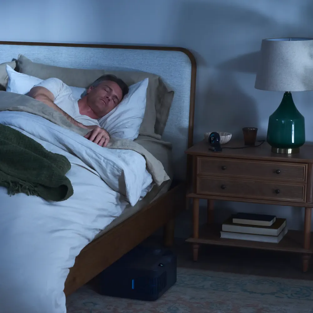 A man asleep in a cool, dark bedroom on a Chilipad covered mattress