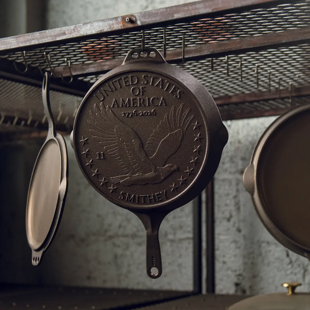 A Smithey cast iron skillet hanging on a metal rack, its cast eagle medallion catching the light.