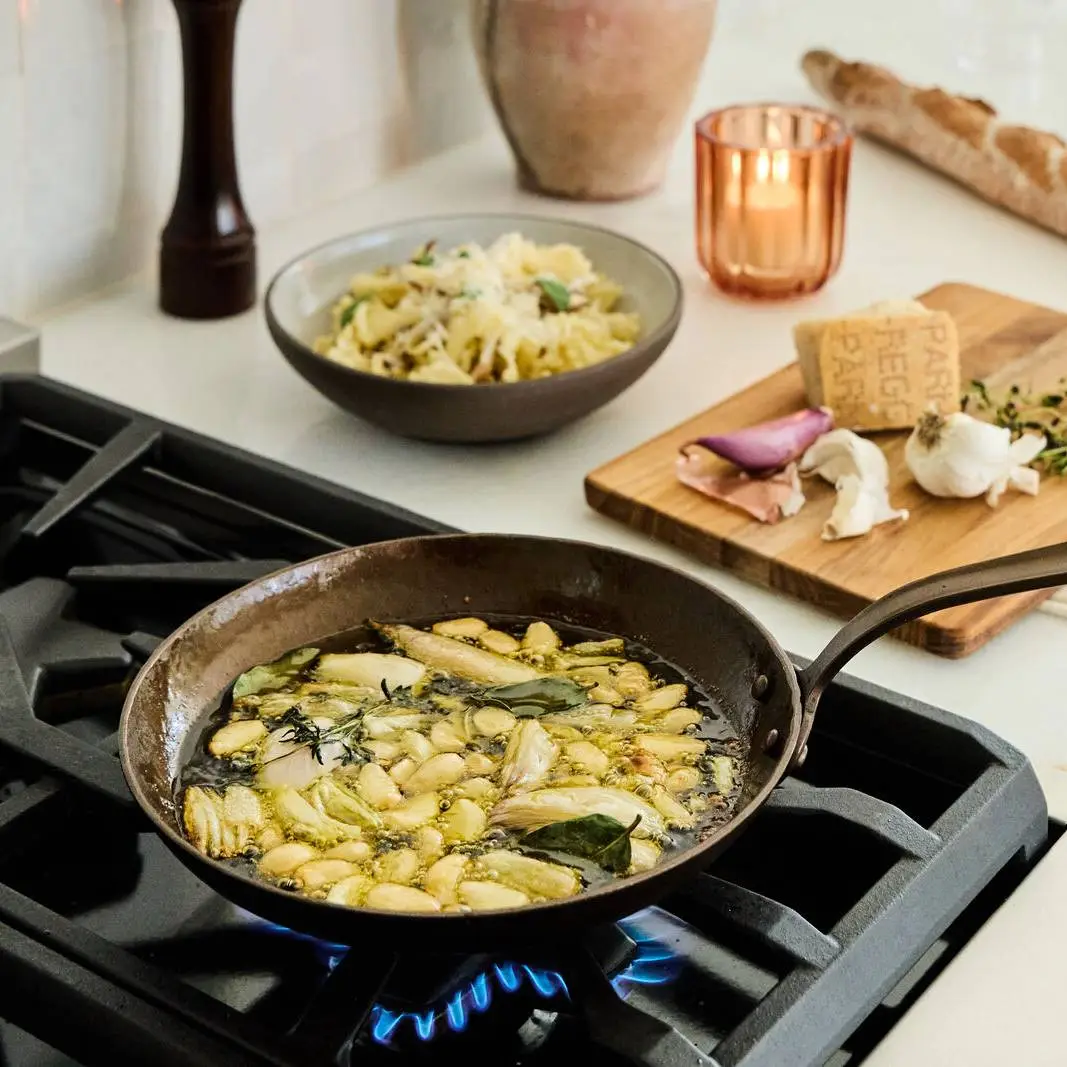 A hand forged carbon steel Smithey skillet cooking pasta on a lit gas burner in a home kitchen.