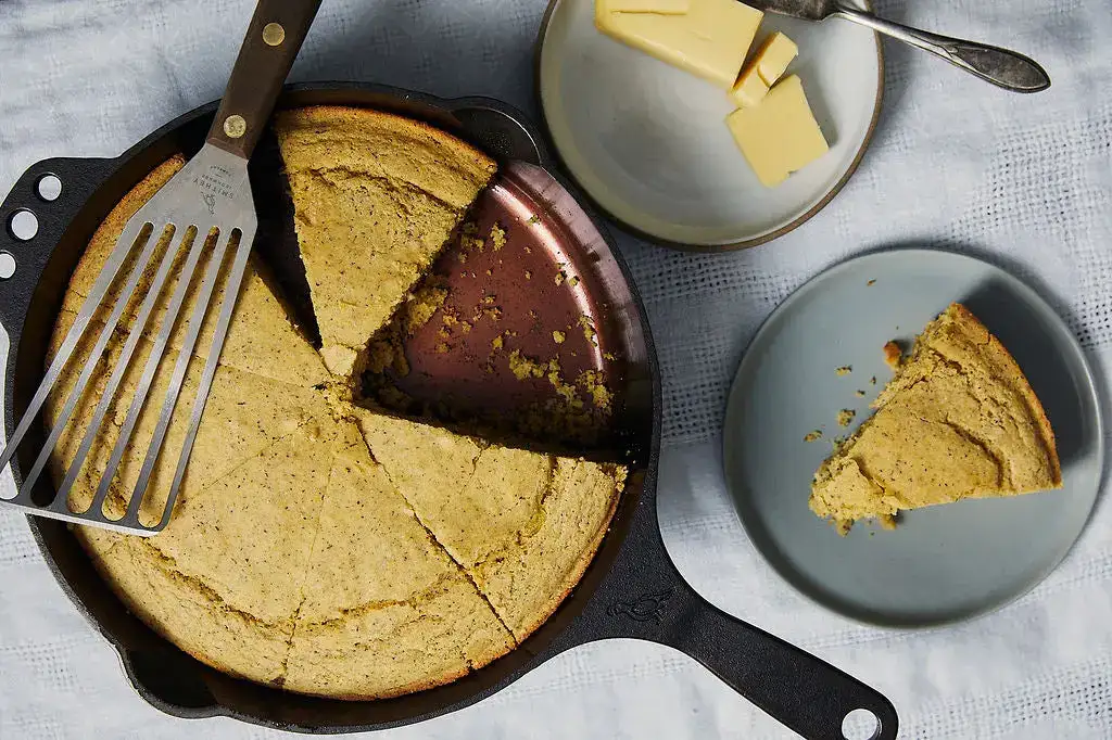 Skillet cornbread cut into wedges in a Smithey cast iron pan, with butter alongside.