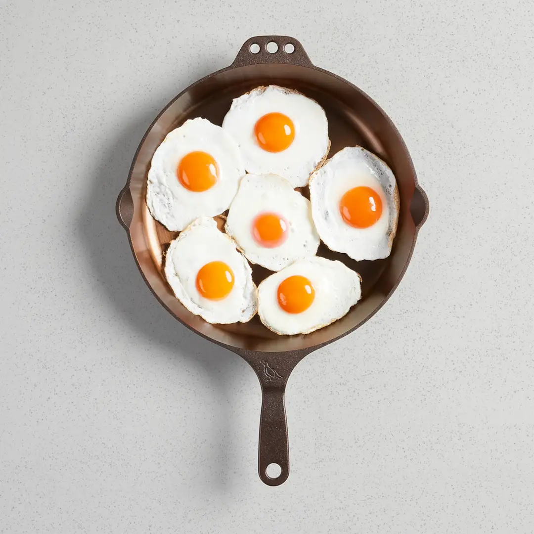 Six fried eggs cooked together in a Smithey cast iron skillet, each one separate and intact.