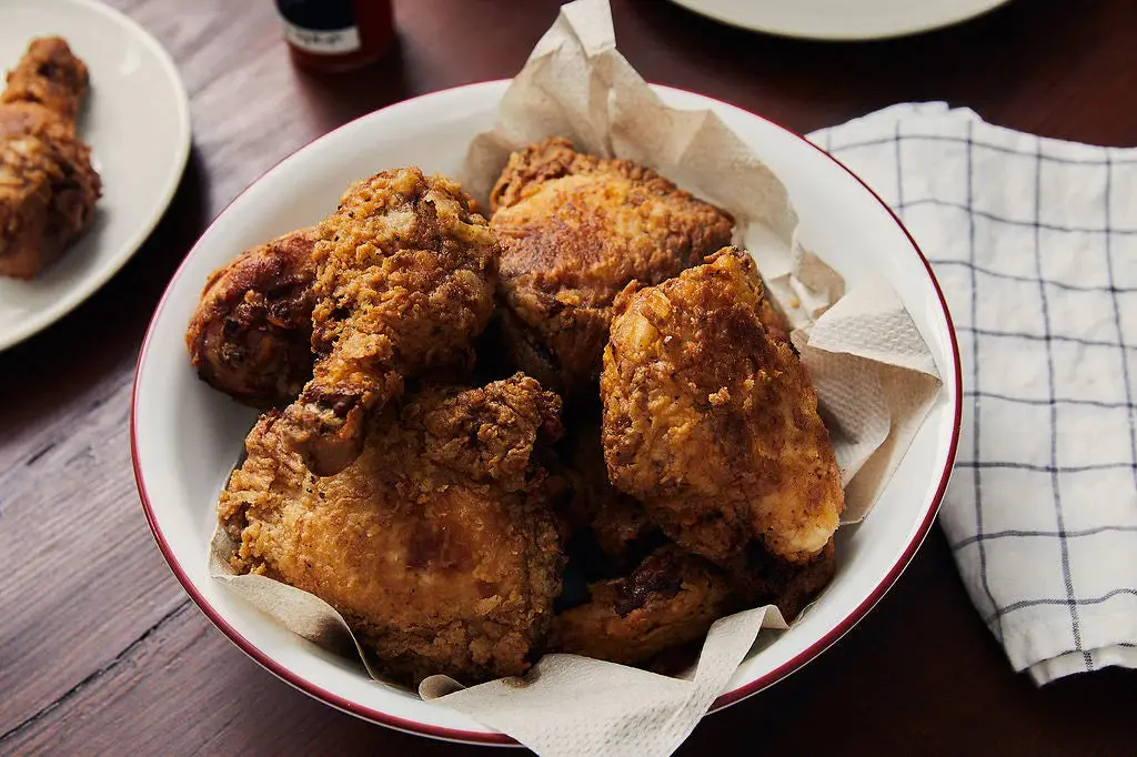 A bowl of fried chicken next to a checked cloth, cooked in cast iron.