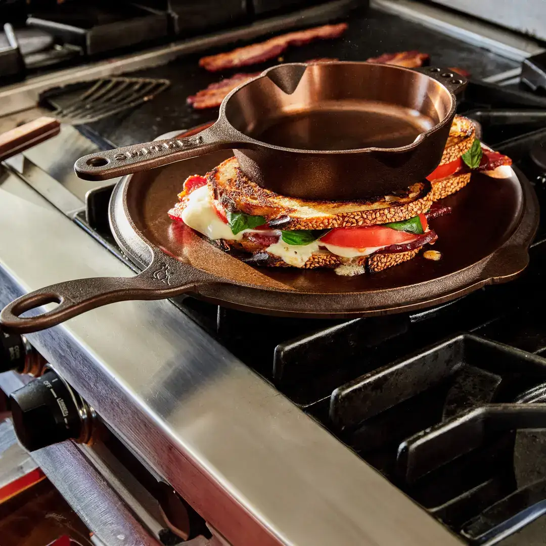 A Smithey cast iron griddle in use on a gas range with breakfast cooking on it.