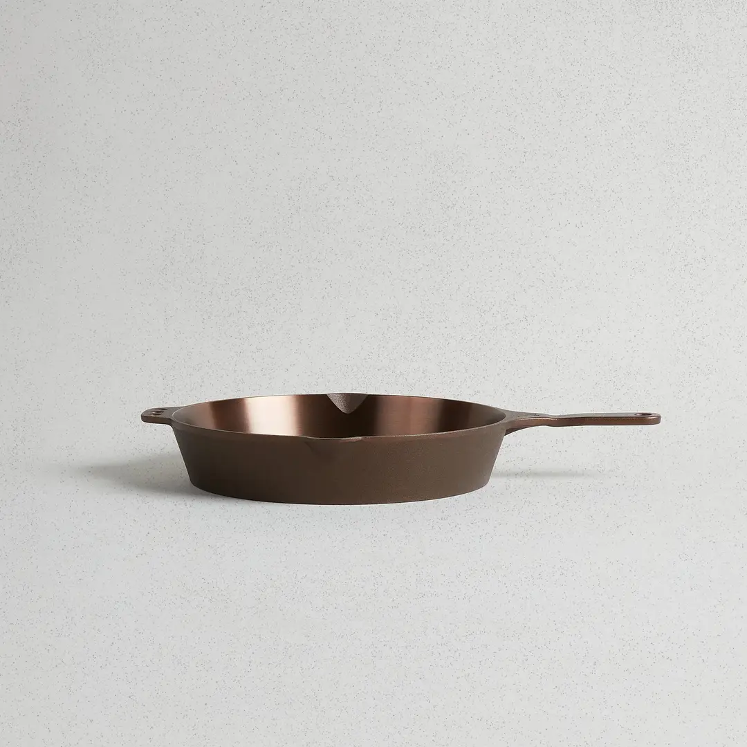 A Smithey No. 12 cast iron skillet seen at an angle, showing its bronze polished interior and long handle.