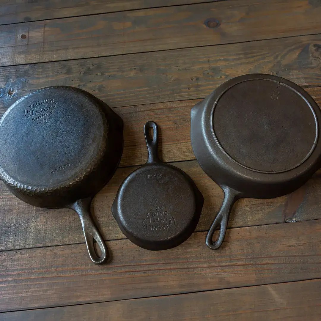 Three restored cast iron skillets laid out on a dark wooden surface after refinishing.
