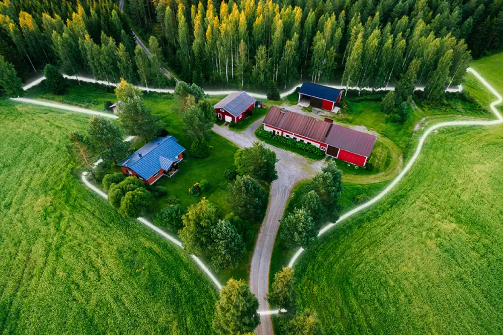 Aerial photograph of a farmstead with red barns surrounded by forest, with a glowing line marking the property boundary