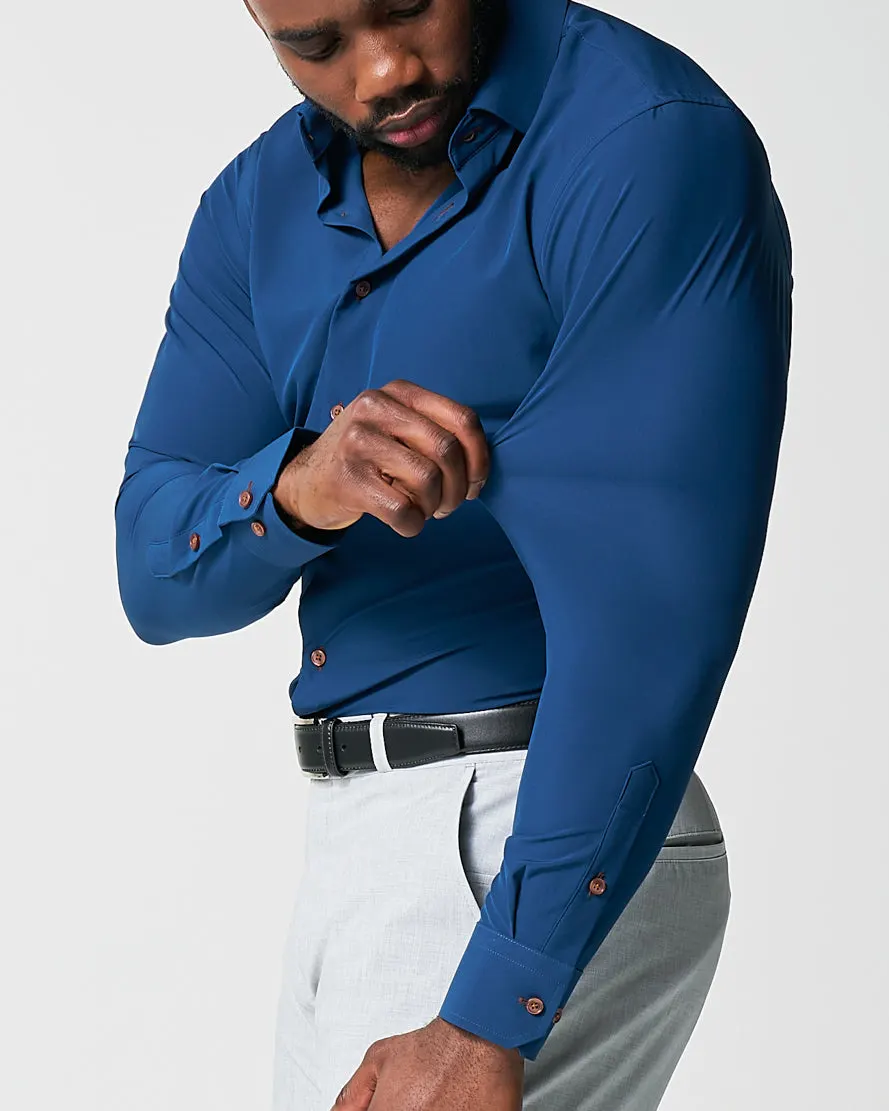 A man reaching across his body in a navy State and Liberty dress shirt, the fabric following the arm