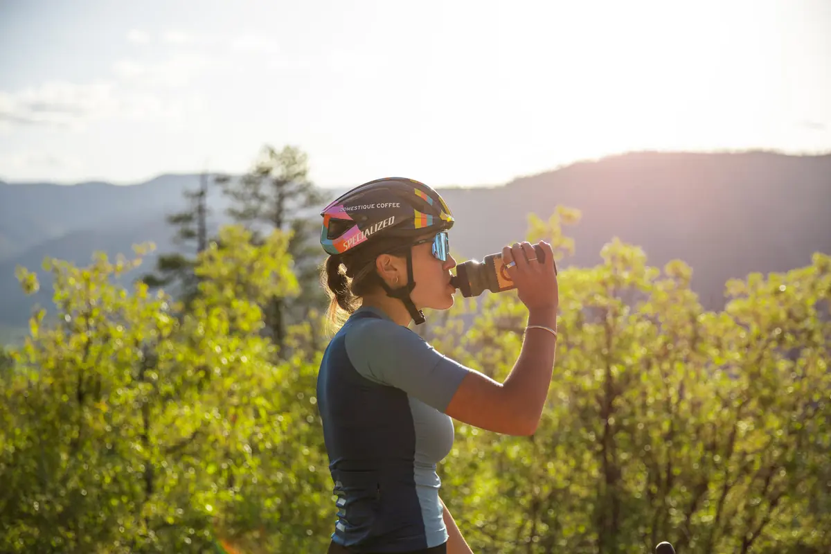 Cyclist drinking from a bottle on a dirt road at sunset with mountains behind
