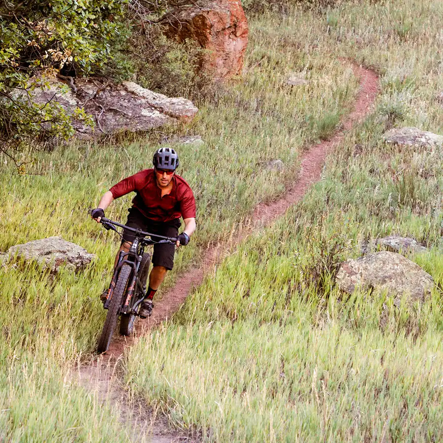 Mountain biker riding singletrack through a green mountain meadow