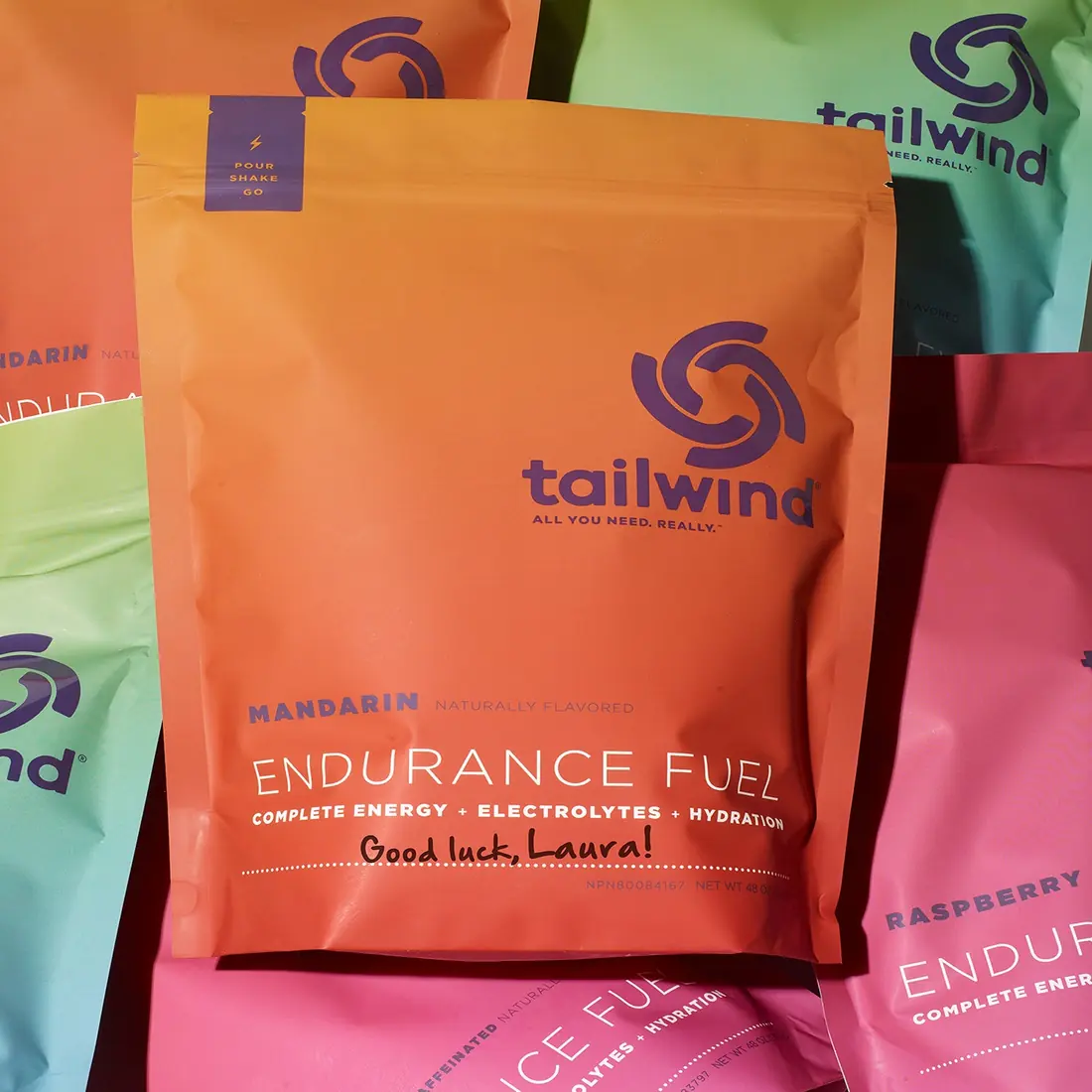 A Tailwind Endurance Fuel Mandarin single serving packet with Good luck, Laura! handwritten on it, among other flavor packets