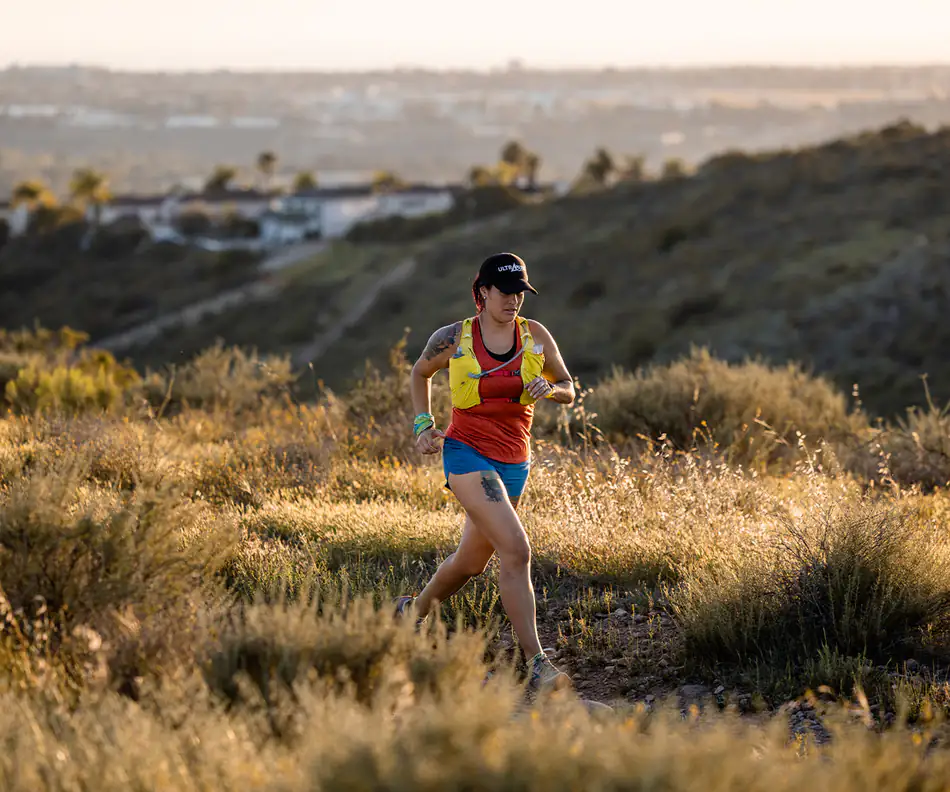 Trail runner on a narrow path through dry golden hills in strong afternoon light