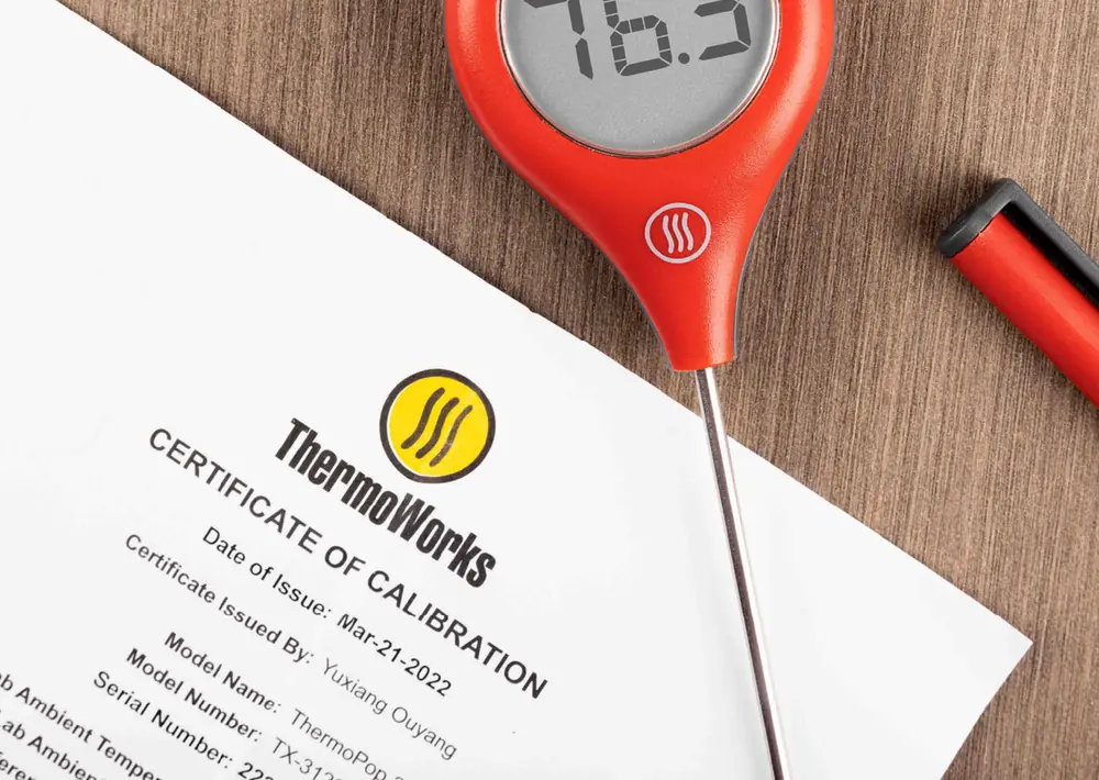 A red ThermoPop thermometer reading 76.3 degrees lying on a ThermoWorks Certificate of Calibration showing date of issue, model name and serial number