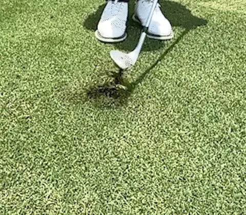 A traditional wedge digging into the turf behind the ball, throwing up a divot while the ball stays put