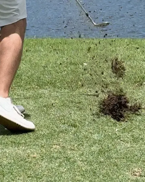 A large divot flying after a conventional wedge digs into the turf beside water