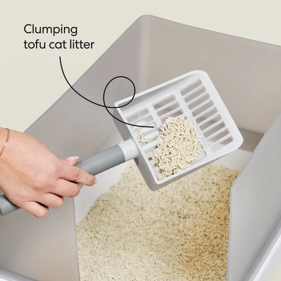 A slotted scoop lifting a clump out of a bed of pale tofu litter pellets