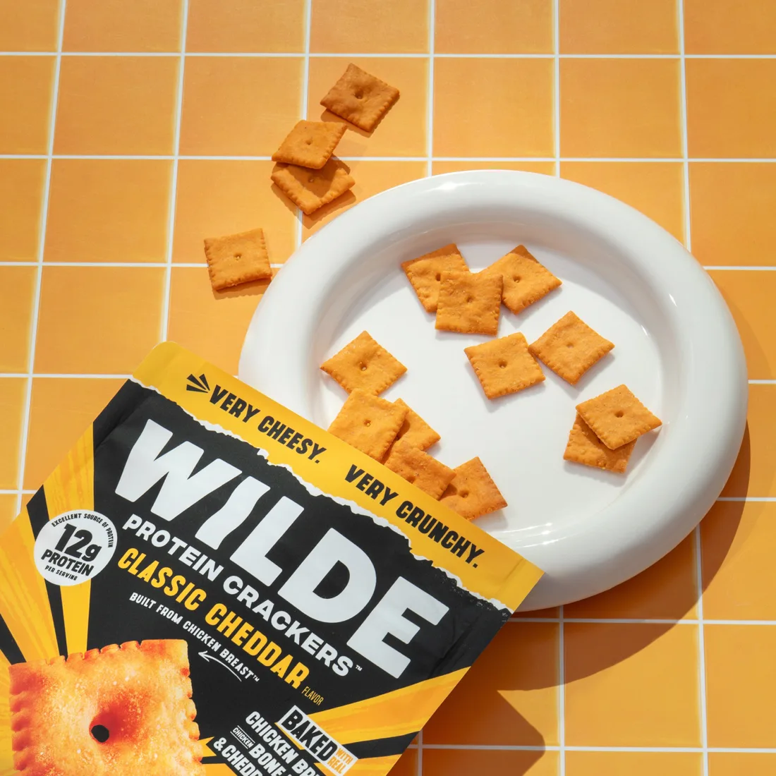 WILDE Protein Crackers Classic Cheddar poured onto a white plate next to the bag
