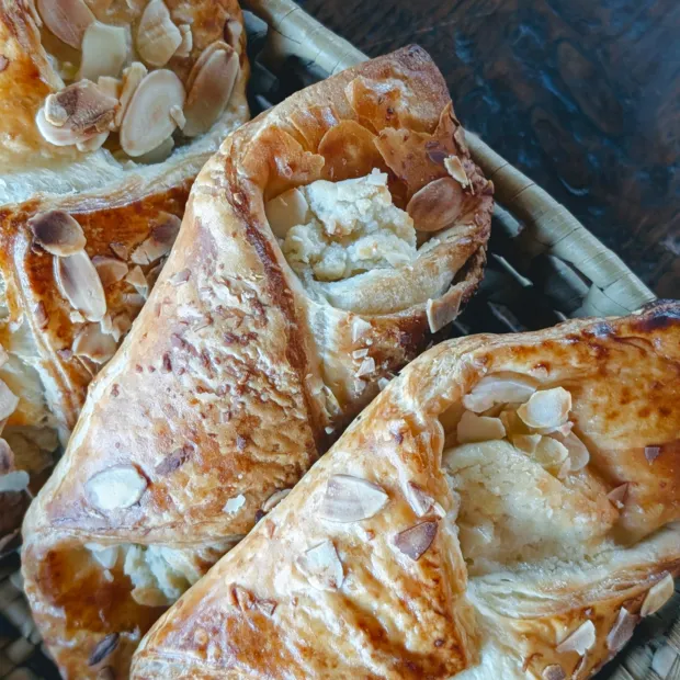Almond croissants topped with flaked almonds and icing sugar in a lined baking tray