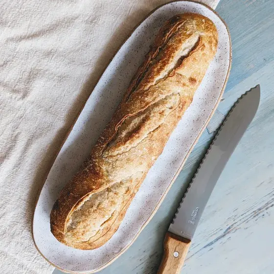A sourdough demi baguette on a metal tray beside a bread knife