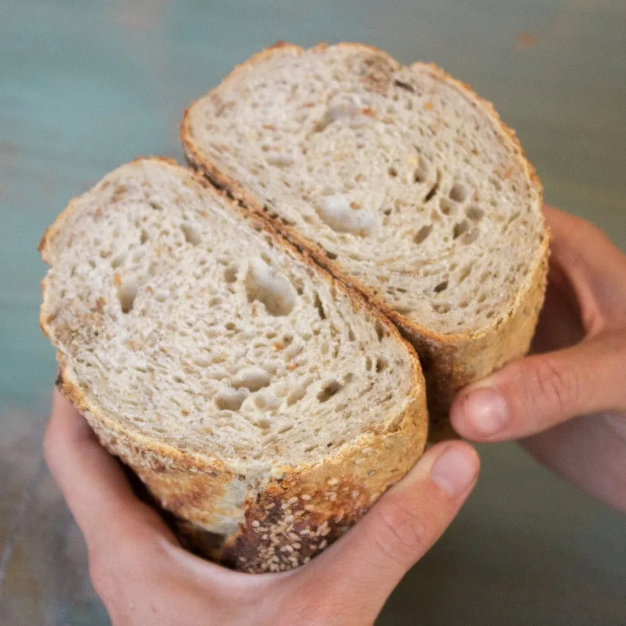 Two hands holding an open sourdough loaf, the irregular open crumb visible across both cut faces