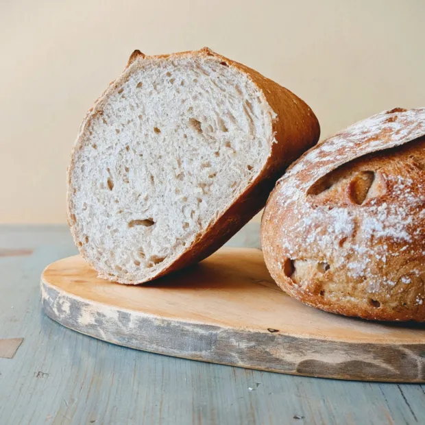 Two round gluten-free sourdough loaves on a wooden board, one cut open to show the crumb