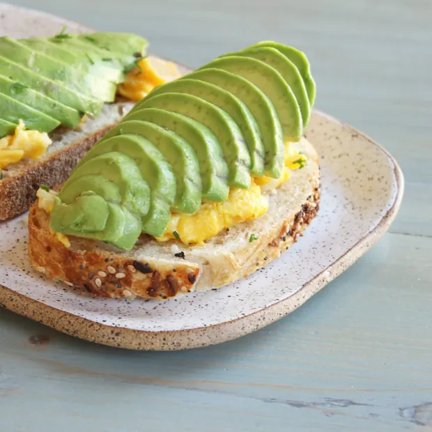 Sliced avocado and scrambled egg on a thick slice of toasted sourdough, on a ceramic plate