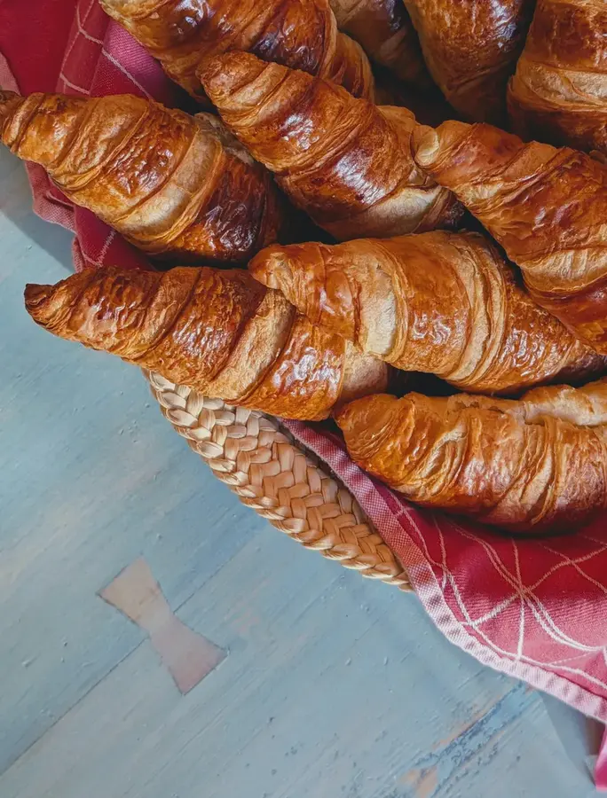 Golden croissants with visible spiral layering, arranged on a red patterned cloth in a woven basket