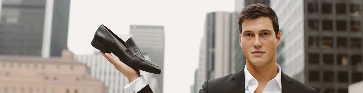 A man in a suit on a city street holding a traditional leather dress shoe